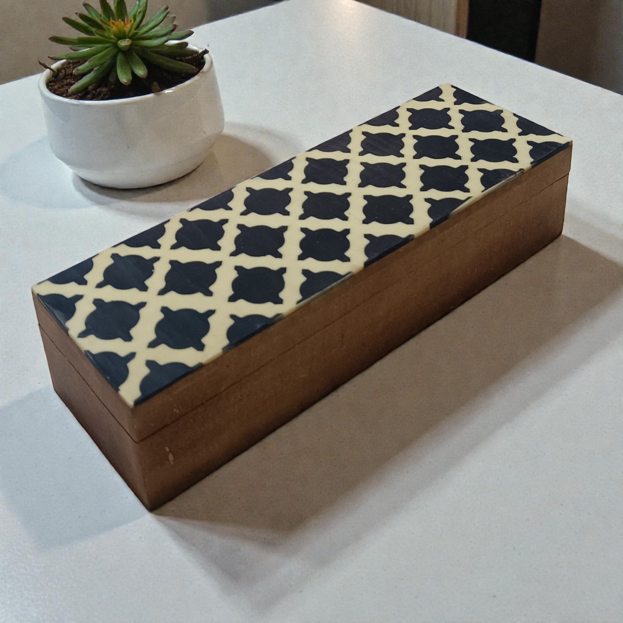  Wooden box with geometric pattern on a white surface next to a potted plant 