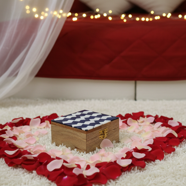  Romantic setup with heart-shaped rose petals, a checkered box, a rose, a cup of coffee, and a letter on a white carpet. 